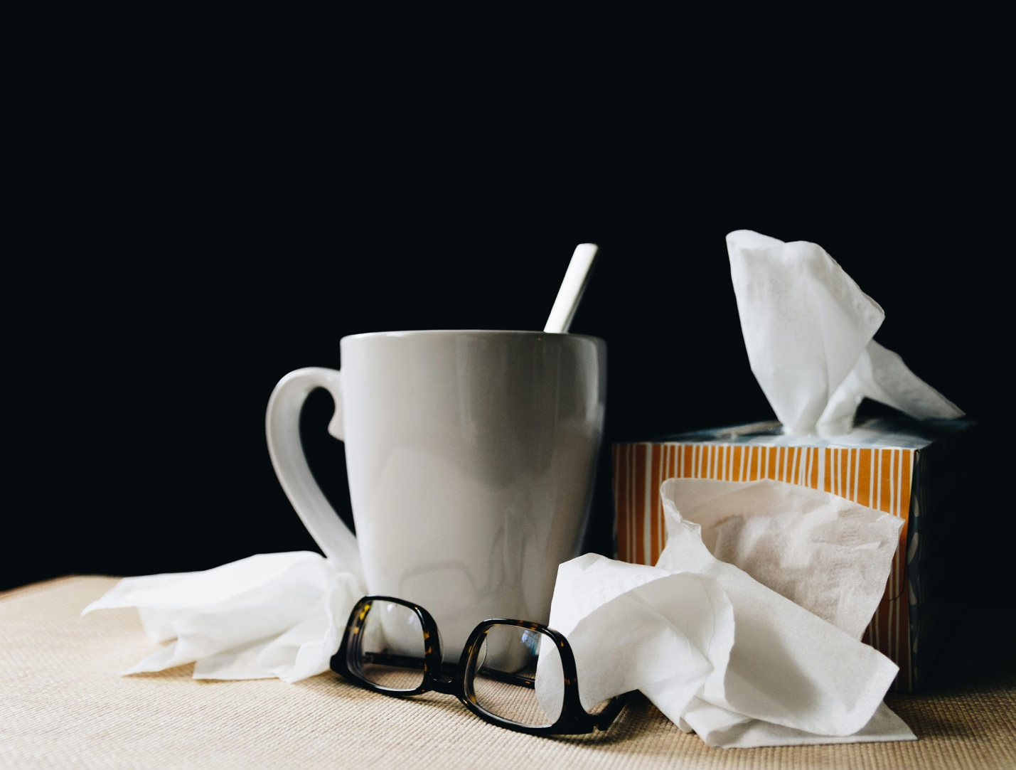 A photo of a white mug, a box of tissues, and glasses on a table.