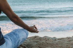 A person meditating on a beach, with the ocean waves in the background.